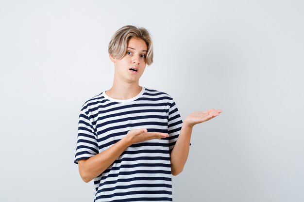 Teen boy faisant semblant de montrer quelque chose en t-shirt et l'air perplexe. vue de face.