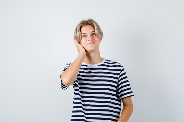 Teen boy gardant la main sur la tête en t-shirt et l'air joyeux, vue de face.