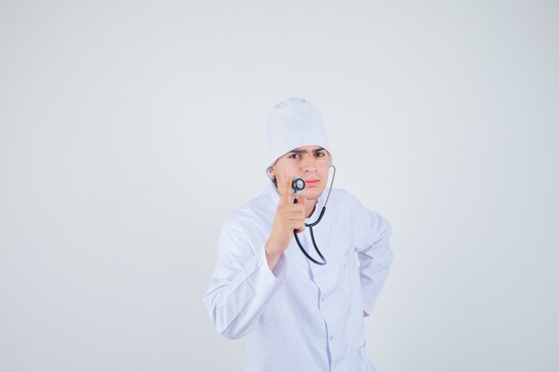 Teen boy holding stéthoscope tout en faisant semblant de vérifier le rythme cardiaque en uniforme de médecin et à la grave