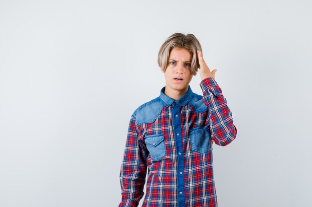 Teen boy avec la main sur la tête en chemise à carreaux et à la grave , vue de face.