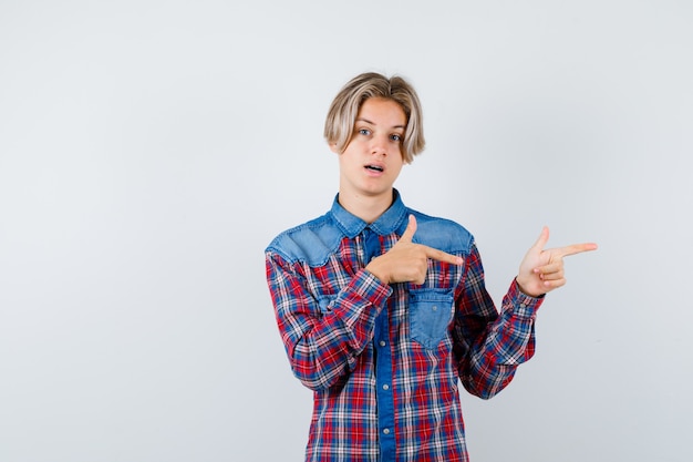 Teen boy pointant vers le côté droit en chemise à carreaux et l'air perplexe. vue de face.