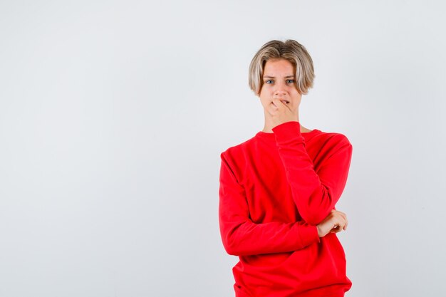 Teen boy se ronger les ongles en pull rouge et à l'aise , vue de face.