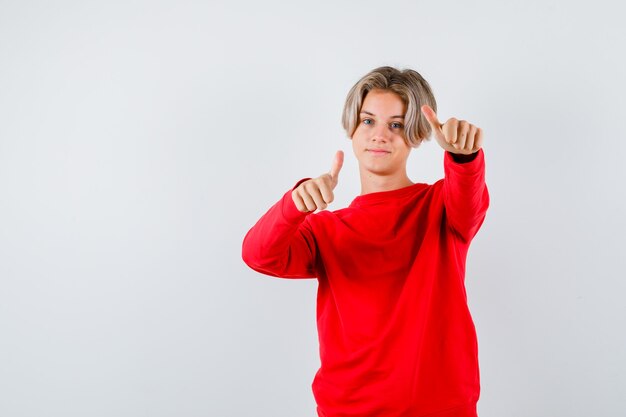 Teen boy showing Thumbs up en pull rouge et l'air satisfait. vue de face.