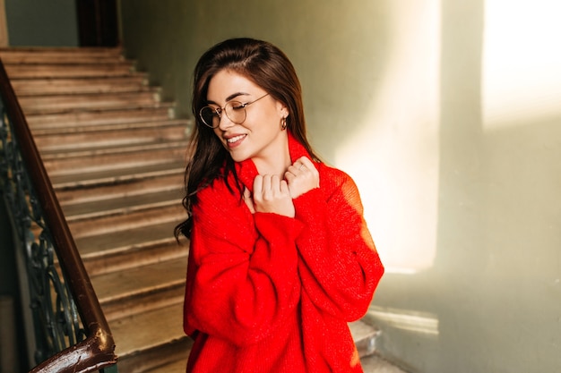 Teen fille dans des verres sur le mur des escaliers. Le mannequin aux cheveux longs sourit doucement, tenant son pull brillant.