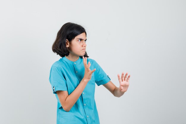 Teen girl en chemise bleue levant les mains de manière agressive et à la colère