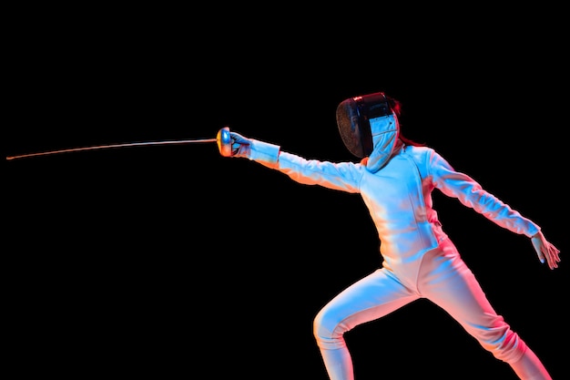 Photo gratuite teen girl en costume d'escrime avec l'épée à la main isolé sur fond noir, néon.