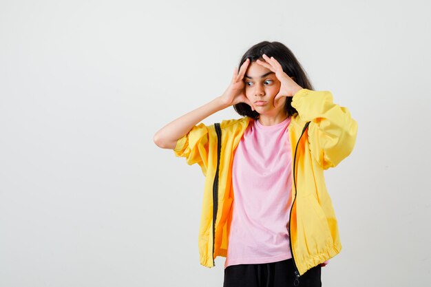 Teen girl gardant les mains sur le visage en t-shirt, veste et l'air pensif , vue de face.