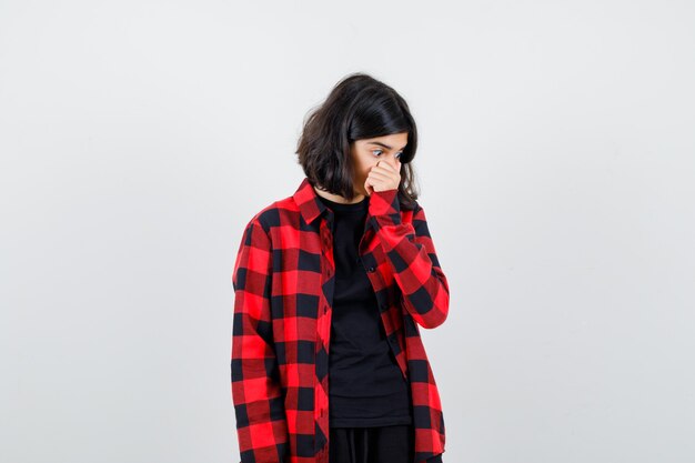 Teen girl holding hand on face in casual shirt et l'air choqué, vue de face.