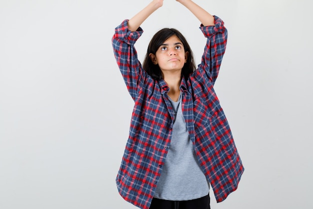 Teen Girl In Checkered Shirt Faisant Le Geste Du Toit De La Maison Avec Les Mains Sur La Tête Et à La Nostalgie, Vue De Face. Photo gratuit