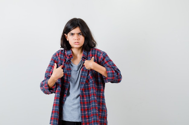 Teen girl in checkered shirt pointant sur elle-même et à la nostalgie, vue de face.
