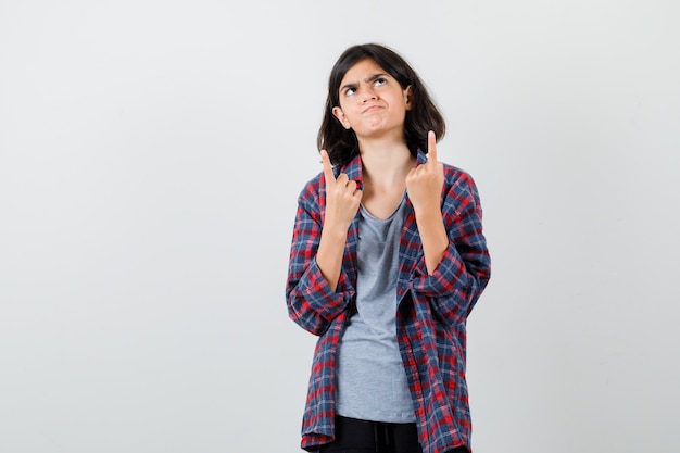 Teen girl pointant vers le haut en chemise à carreaux et l'air insatisfait , vue de face.