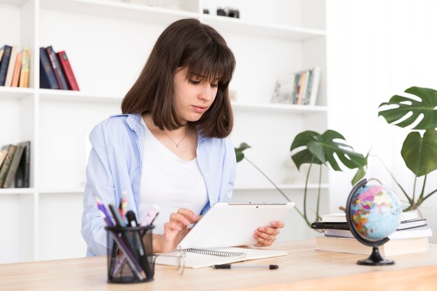 Teenage étudiant assis à table et étudie avec tablette