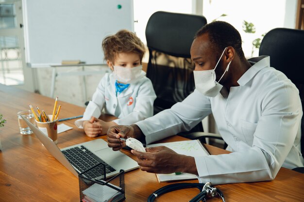 Teenboy caucasien en tant que médecin consultant, donnant des recommandations, traitant. Petit docteur pendant la discussion, étudiant avec un collègue plus âgé. Concept d'enfance, émotions humaines, santé, médecine.