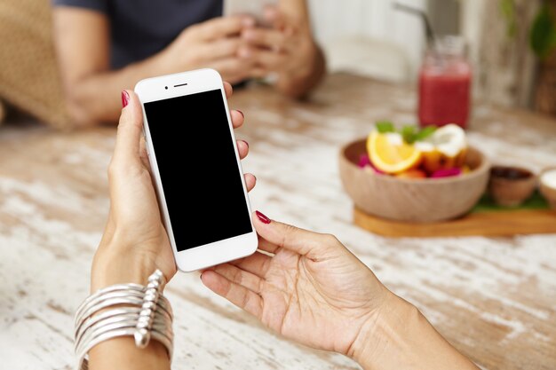 Téléphone intelligent blanc avec écran d'espace copie vierge dans les mains de la femme sur la table de café.