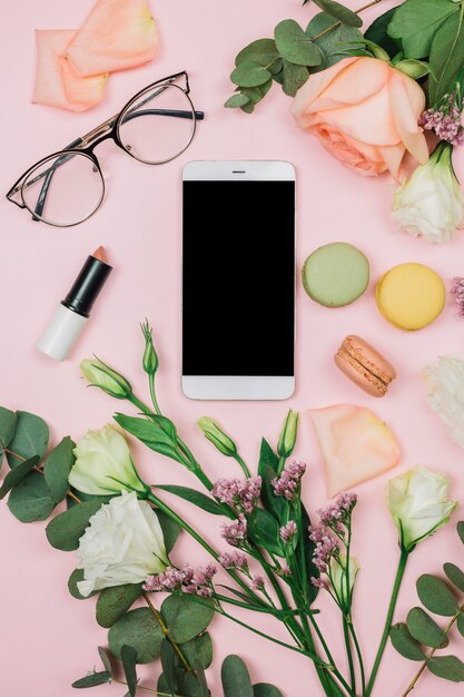 Téléphone intelligent blanc; lunettes; rouge à lèvres ; Rose; fleurs de limonium et d&#39;eustoma sur fond rose