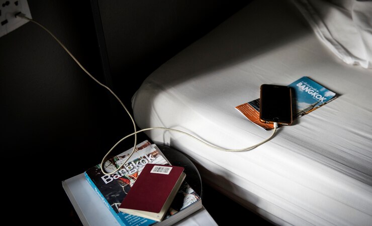 Photo gratuit un téléphone mobile en charge couché sur le lit avec un guide de voyage de bangkok, en thaïlande et une brochure