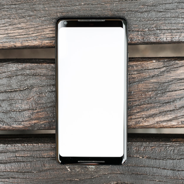 Photo gratuite téléphone portable avec écran blanc sur une planche de bois texturée