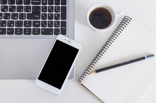 Téléphone portable sur ordinateur portable avec une tasse de café et un crayon sur le cahier