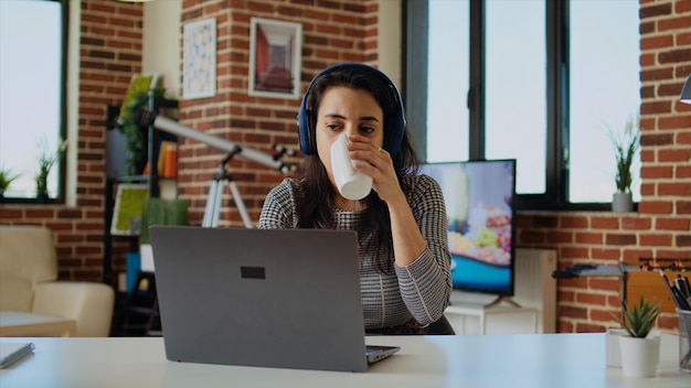 Photo gratuite un télétravailleur vérifie ses courriels sur son ordinateur portable alors qu'il est à son bureau à boire du café.