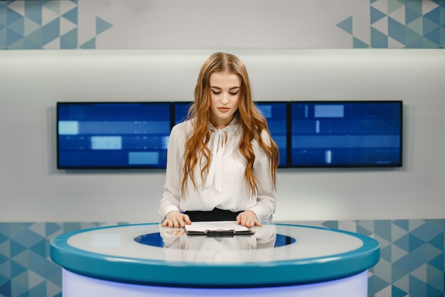 Photo gratuite télévision présente au studio se préparant pour une nouvelle diffusion. jeune fille souriante en chemise blanche assise à table.