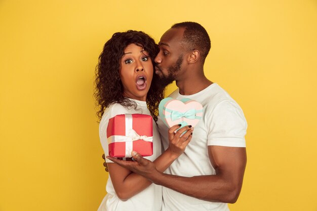 Tenant des coffrets cadeaux. Célébration de la Saint-Valentin, heureux couple afro-américain isolé sur mur jaune. Concept d'émotions humaines, expression faciale, amour, relations, vacances romantiques.