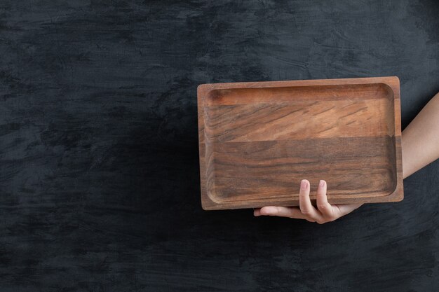 Tenant un plateau en bois carré avec la main