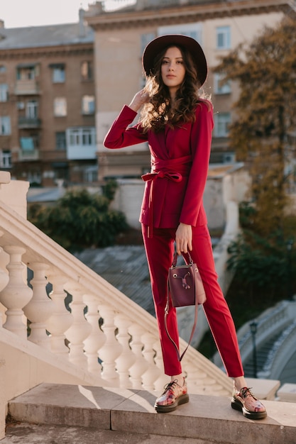 Tendance belle femme élégante en costume violet marchant dans la rue de la ville, tendance de la mode printemps été automne saison portant chapeau, tenant sac à main