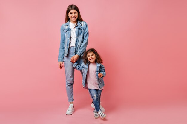 Tendance jeune femme tenant la main avec sa fille bouclée. Photo de Studio d'une maman attarctive et d'un enfant préadolescent dansant ensemble.