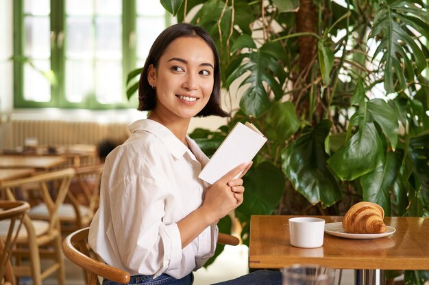 Photo gratuite tendre belle fille asiatique assise avec un livre dans un café lisant et buvant du café et