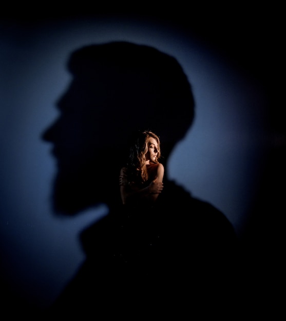 Tendre caucasienne blonde girl avec les yeux fermés est debout dans l'ombre de la tête de l'homme sur le mur bleu