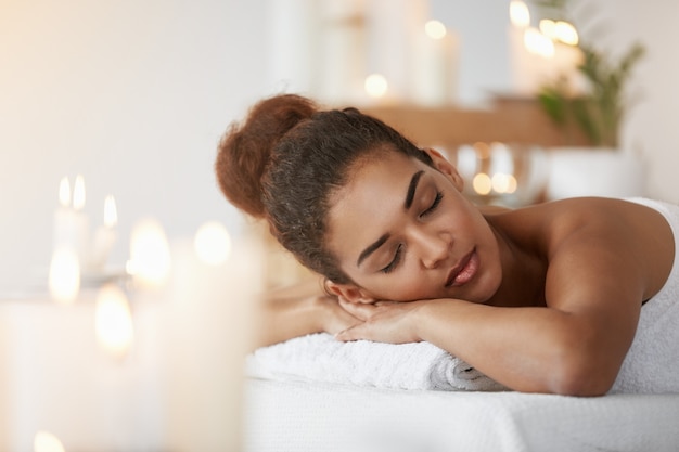 Tendre femme africaine au repos relaxante avec les yeux fermés dans le salon spa.