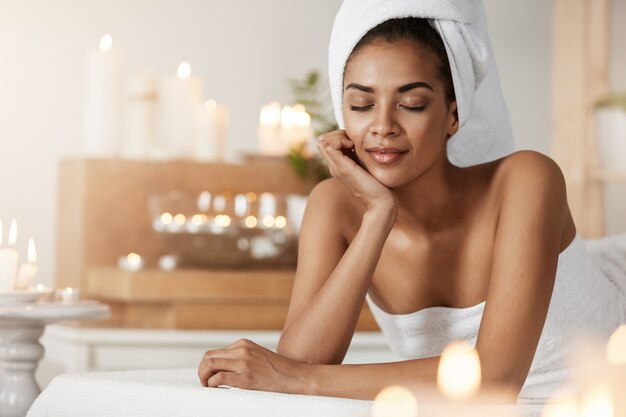 Tendre femme africaine avec une serviette sur la tête reposant de détente dans le salon spa.