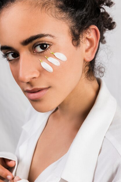 Photo gratuite tendre femme ethnique avec des pétales blancs sur le visage