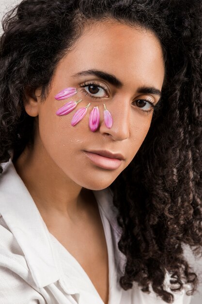 Tendre femme ethnique avec des pétales sur le visage