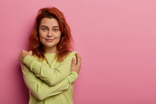 Tendre femme romantique au gingembre se serre dans ses bras, embrasse son propre corps, touche doucement les épaules, a un sourire agréable