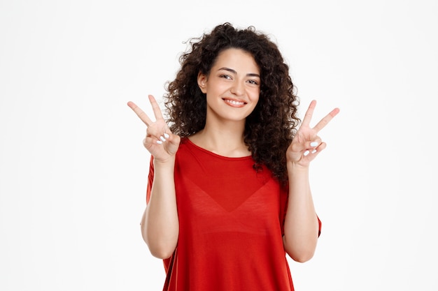 Tendre fille bouclée souriant et montrant le geste de paix