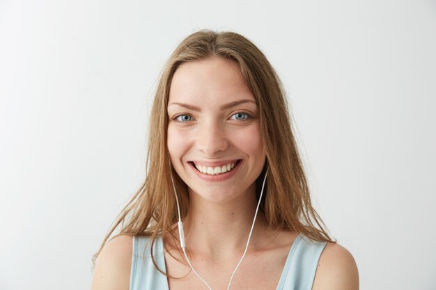 Tendre jeune jolie fille souriante écoutant de la musique en streaming dans les écouteurs.