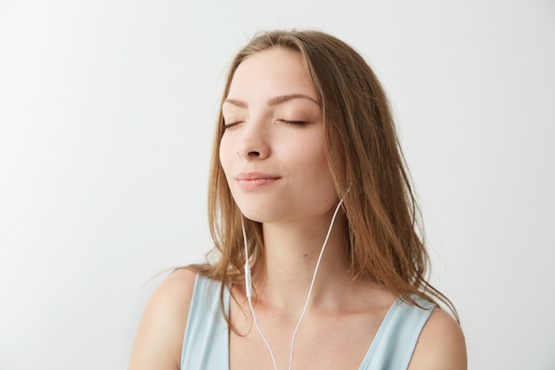 Tendre jeune jolie fille souriante, les yeux fermés, écouter de la musique en streaming dans les écouteurs.