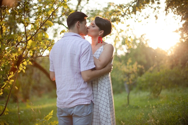 Tendres baisers Couple passionné dans le jardin d'été Jeune homme en chemise légère est debout avec son dos dans le parc d'été avec sa petite amie Le soleil brille vivement sur leurs visages Ils embrassent Gen