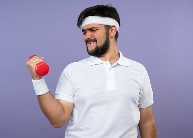 Tense jeune homme sportif portant bandeau et bracelet exercice avec haltère