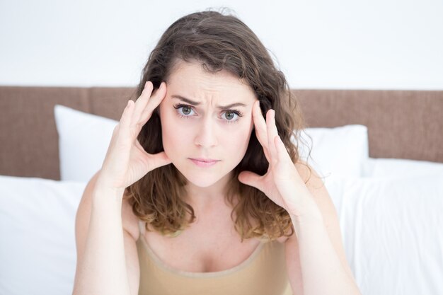 Tensed Beautiful Woman Touching Temples on Bed