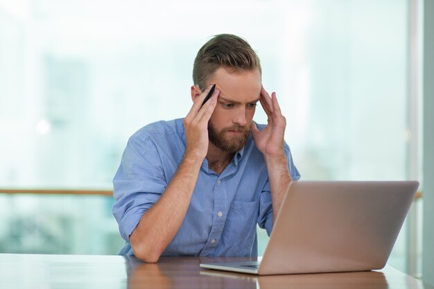 Tensed jeune homme travaillant sur un ordinateur portable au café Table