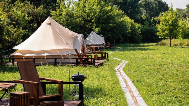 Tentes avec chaises en bois et allée devant elles au glamping. Nature, verdure autour