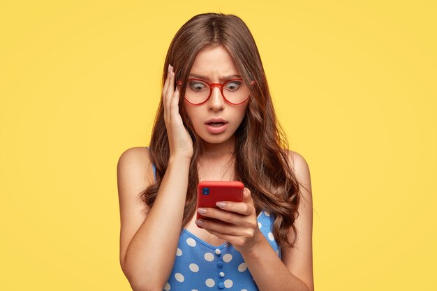 Terrifié jeune femme avec des lunettes posant contre le mur jaune