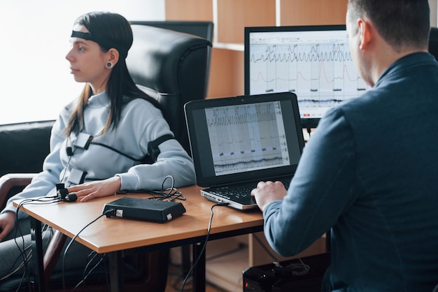 Test de la fidélité de la femme. La fille passe le détecteur de mensonge dans le bureau. Poser des questions. Test polygraphique