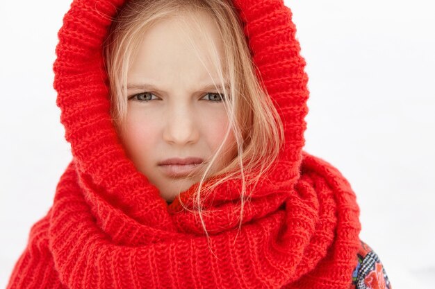 Tête de belle blonde petite fille de race blanche portant une écharpe en laine rouge autour de la tête et du cou