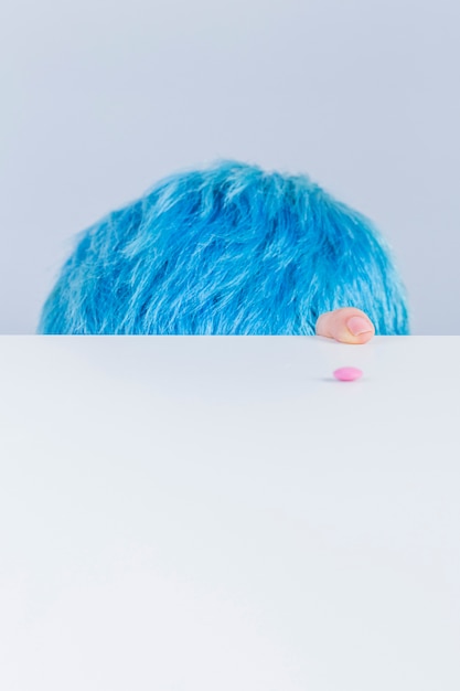 Tête et le doigt de cheveux bleus au bord de la table avec la pilule rose