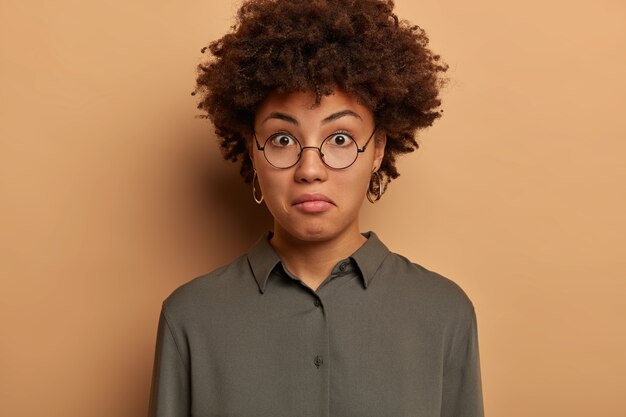 Tête de femme frisée avec une expression émerveillée, exprime la surprise, entend des nouvelles intéressantes, porte des lunettes rondes