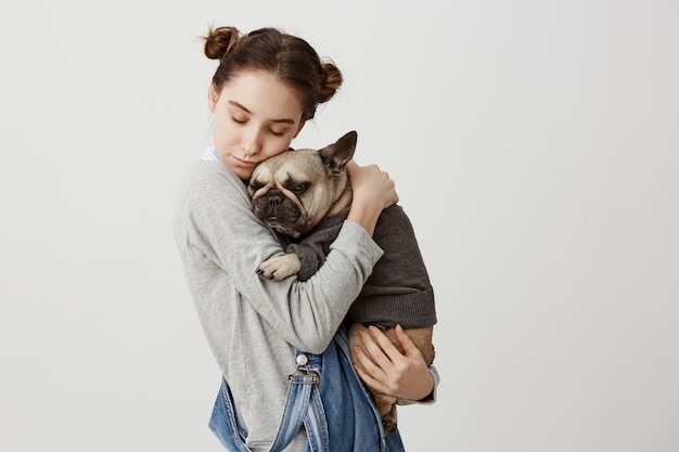 Tête de femme de race blanche avec les yeux fermés tenant son charmant animal de compagnie comme enfant se détendre ensemble. Émotions tendres de jolie fille câlins son petit chien vêtu d'un pull. Soins, concept d'amour