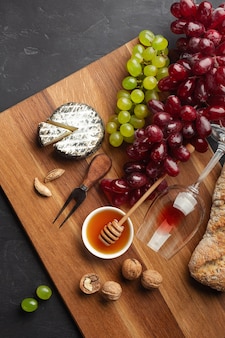 Tête de fromage, grappe de raisin, miel, noix et verre à vin sur planche de bois et fond noir. vue de dessus avec espace de copie.